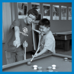 Older boy teaching younger boy to play pool